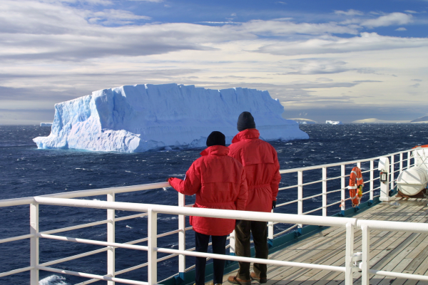A couple in red jackets staring out at icebergs from an Antarctic cruise ship