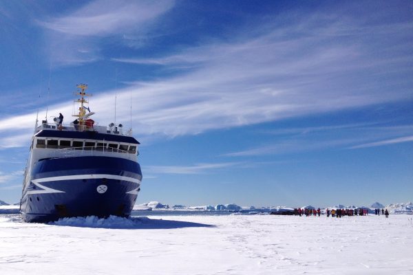 A ship moored in the ice in Antarctica with passengers exploring on the ice